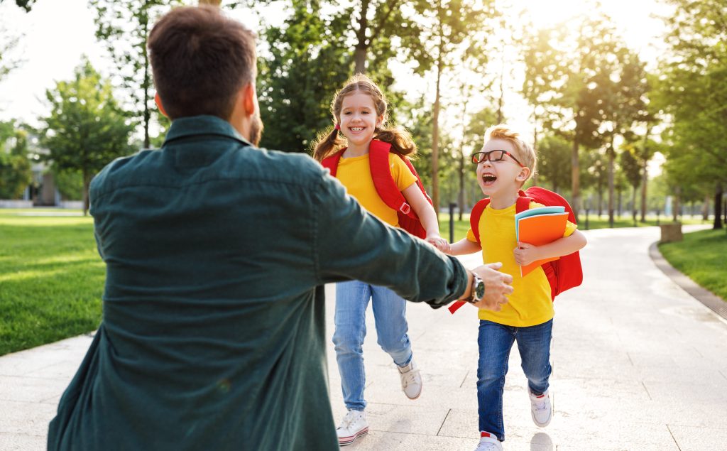 Two children running towards a parent who is waiting to hug them.