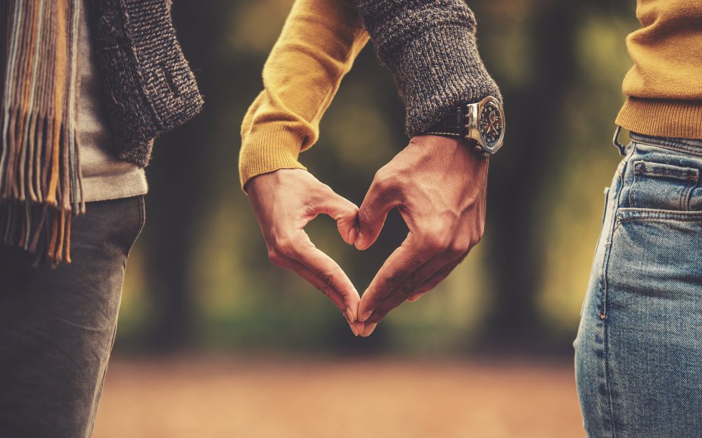 A couple makes a heart out of their hands.