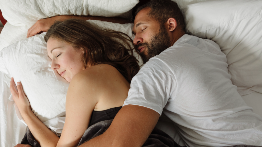 A woman and man cuddle while sleeping in bed.