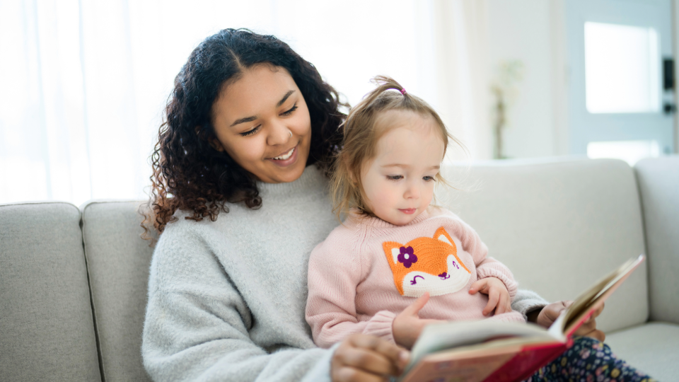 A teenager reads a book with a young child.