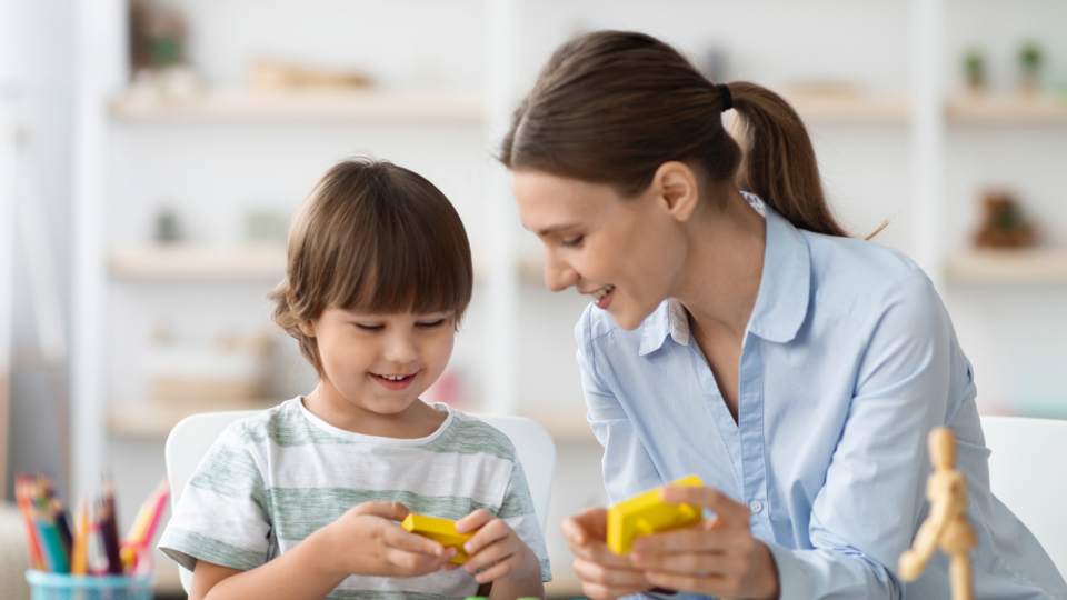 An early childhood educator works with a young child at a table.