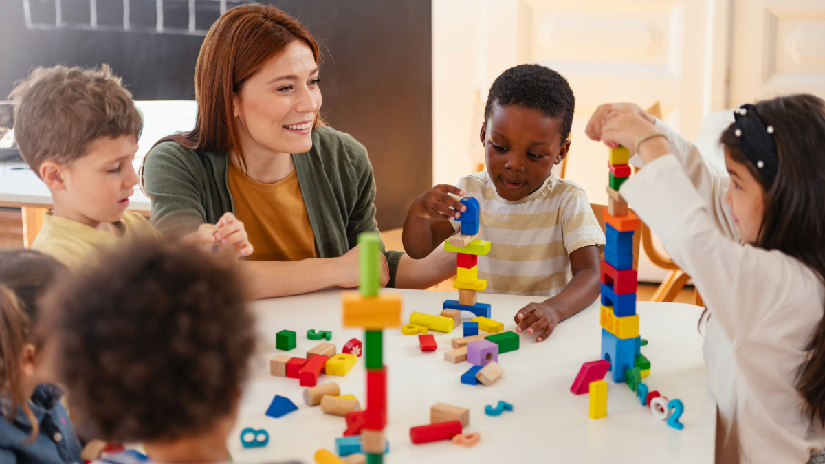 An early childhood professional works with young children at at table.